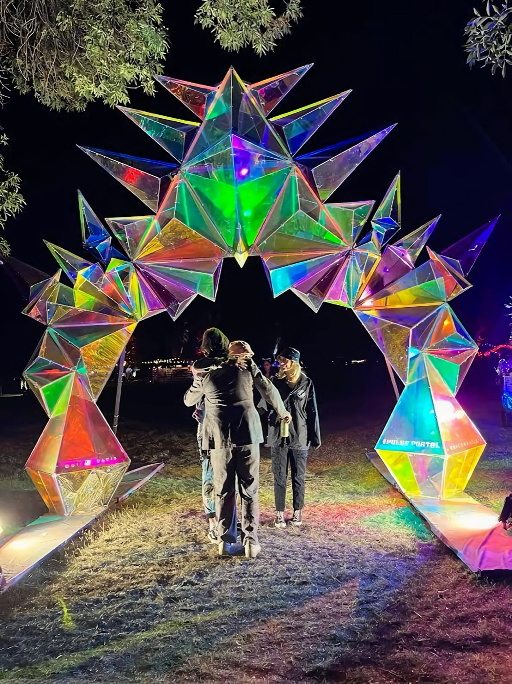 Two people hugging under a glowing iridescent crystal arch at night